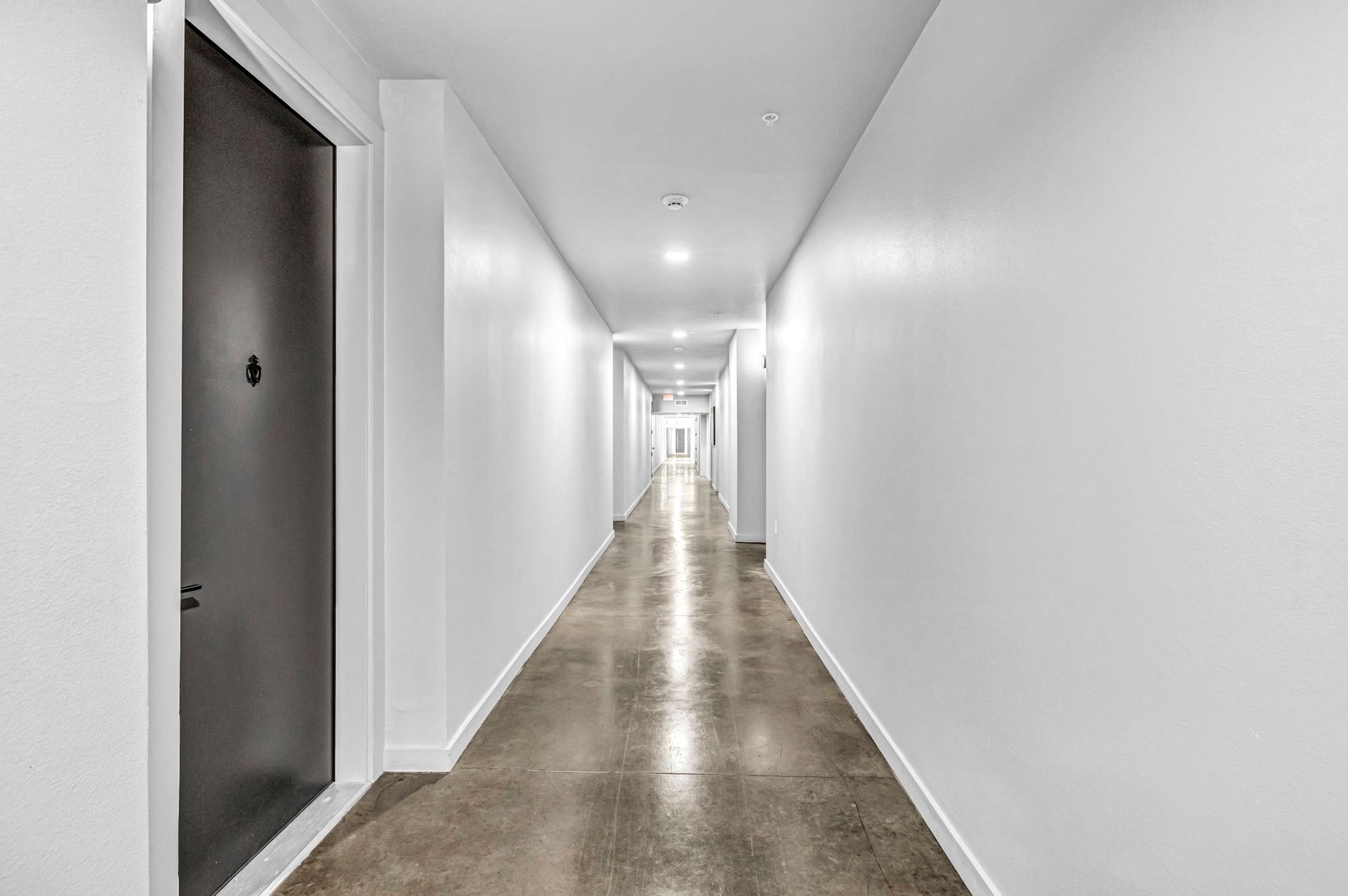 Long, empty white hallway with polished concrete floor and recessed ceiling lights