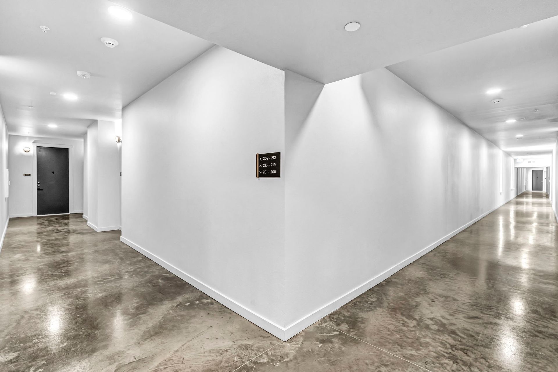 Empty white hallway with polished concrete floor and recessed ceiling lights, branching into two corridors