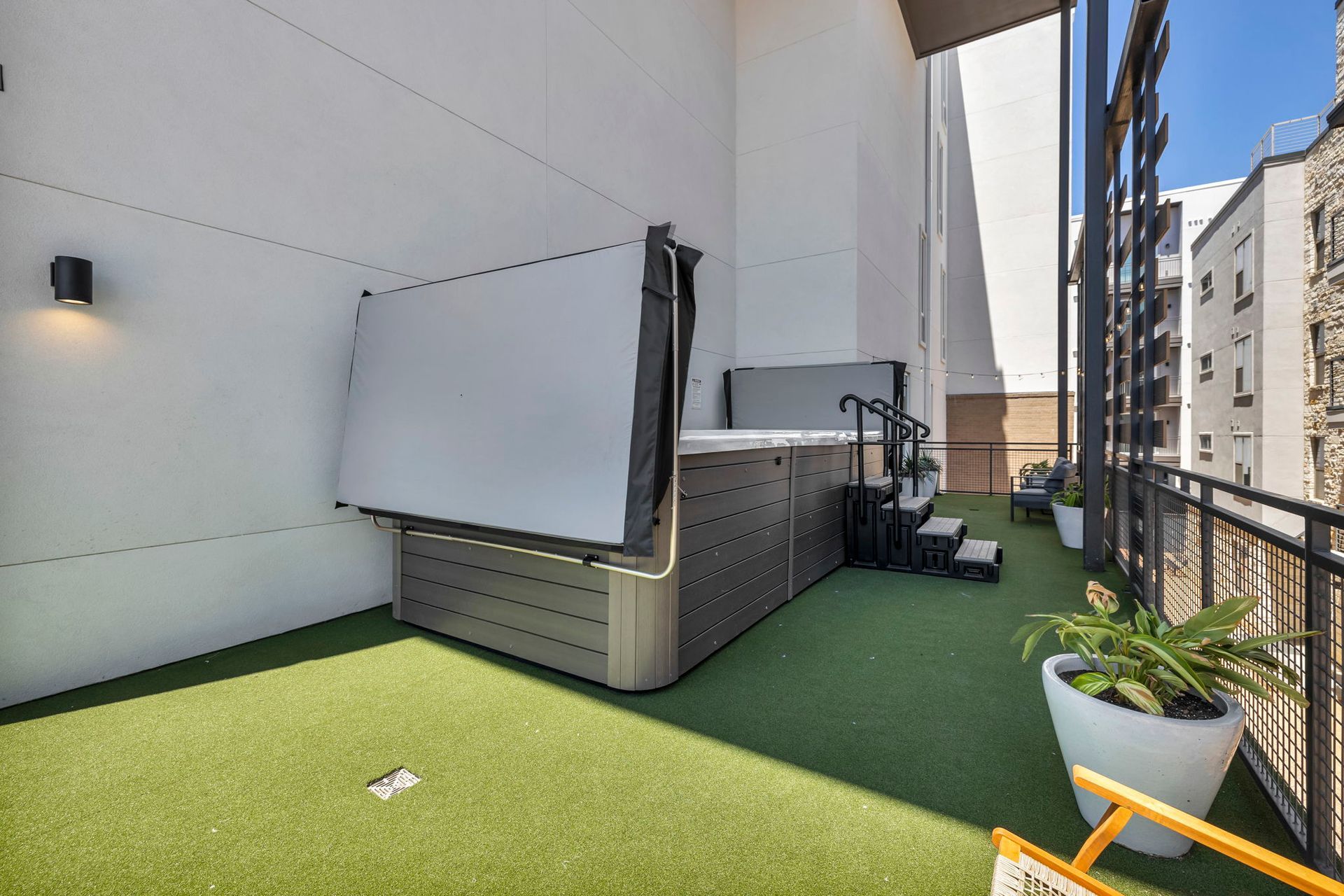 Rooftop terrace with green turf, lounge chairs, planters, and tall white building walls