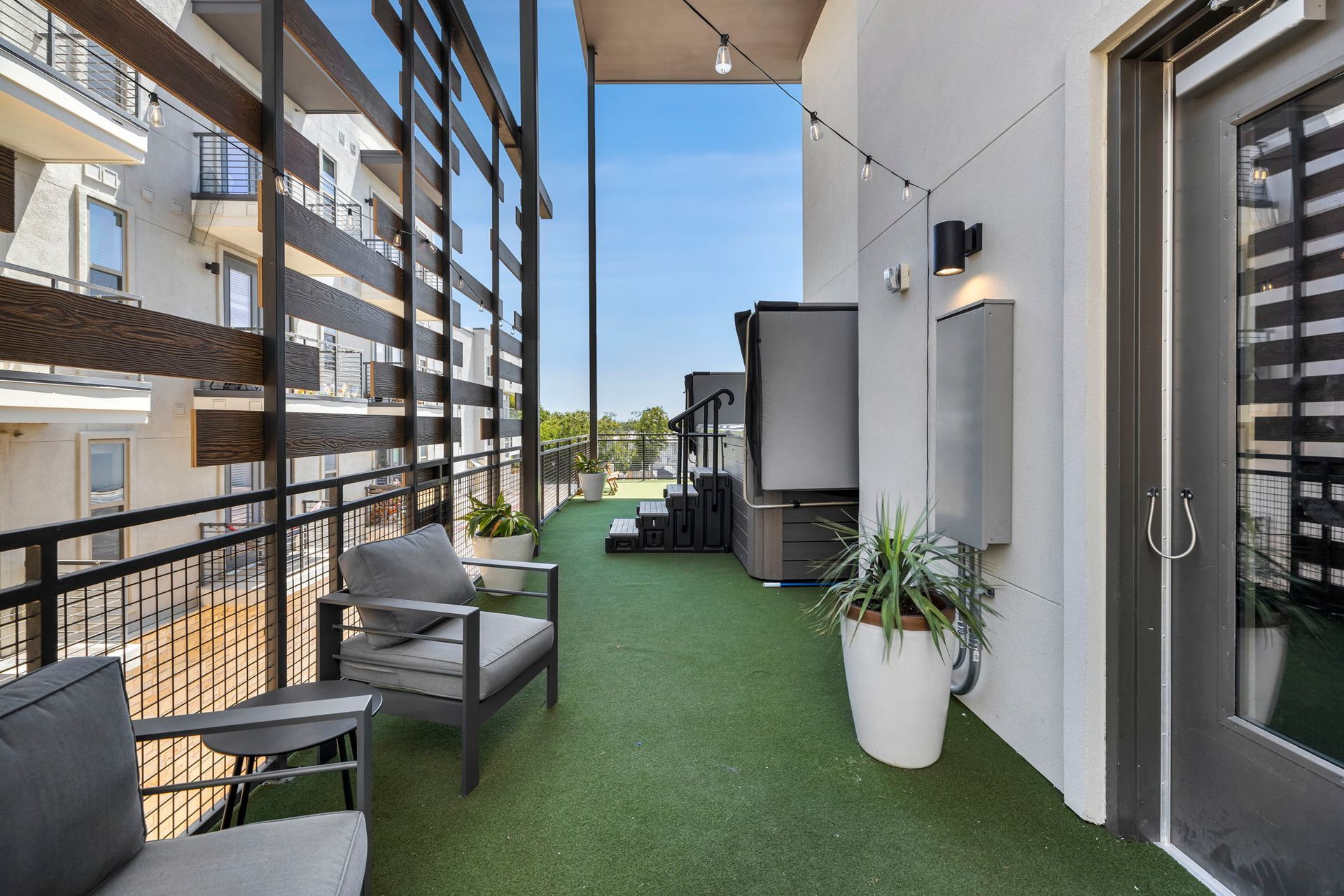 Outdoor apartment balcony with artificial grass, chairs, and potted plants beside neighboring buildings