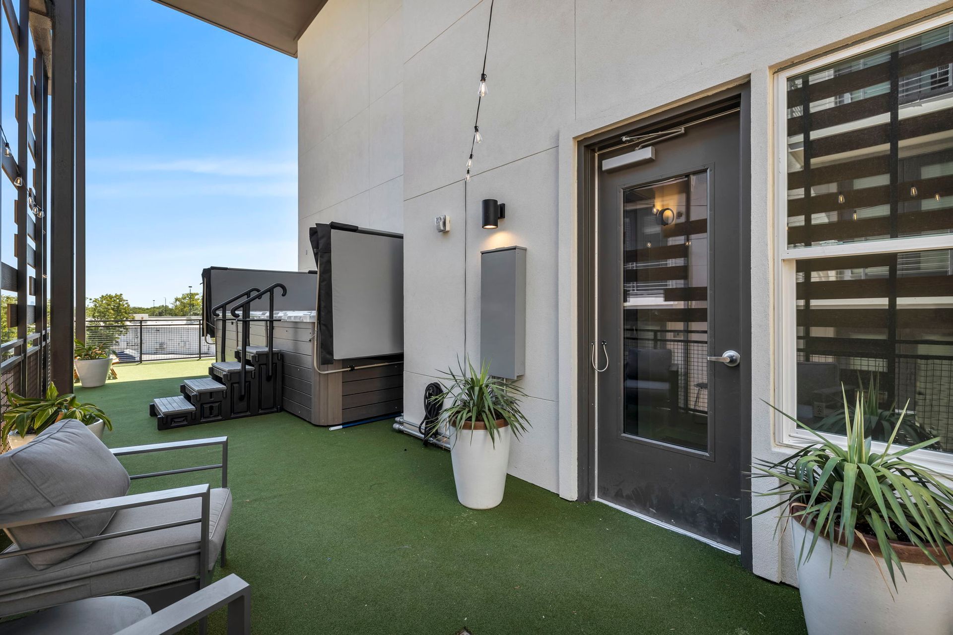 Modern apartment patio with artificial grass, outdoor seating, potted plants, and a glass door