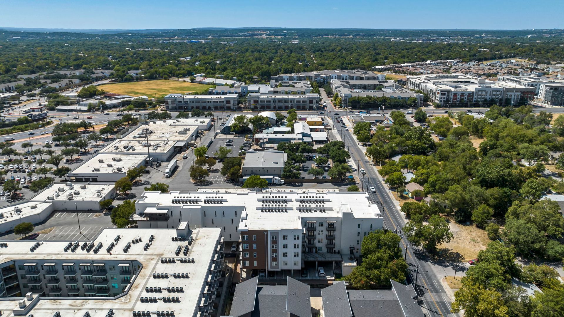 Aerial view of a suburban neighborhood with apartment buildings, tree-lined streets, and distant city skyline