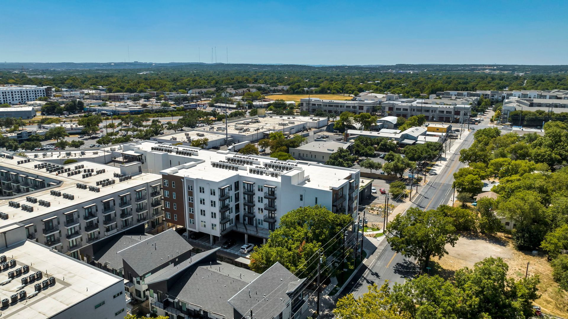 Aerial view of white apartment buildings and tree-lined streets in a sunny neighborhood