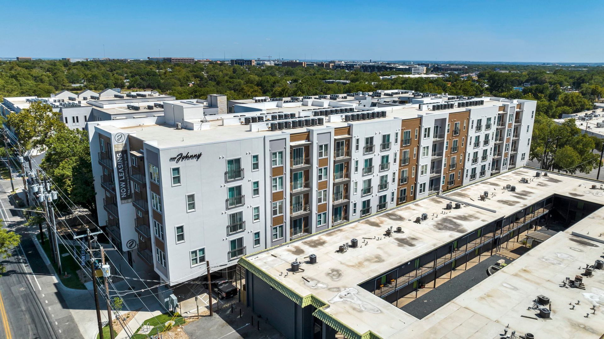 Aerial view of a modern white apartment building with balconies and a large parking lot.
