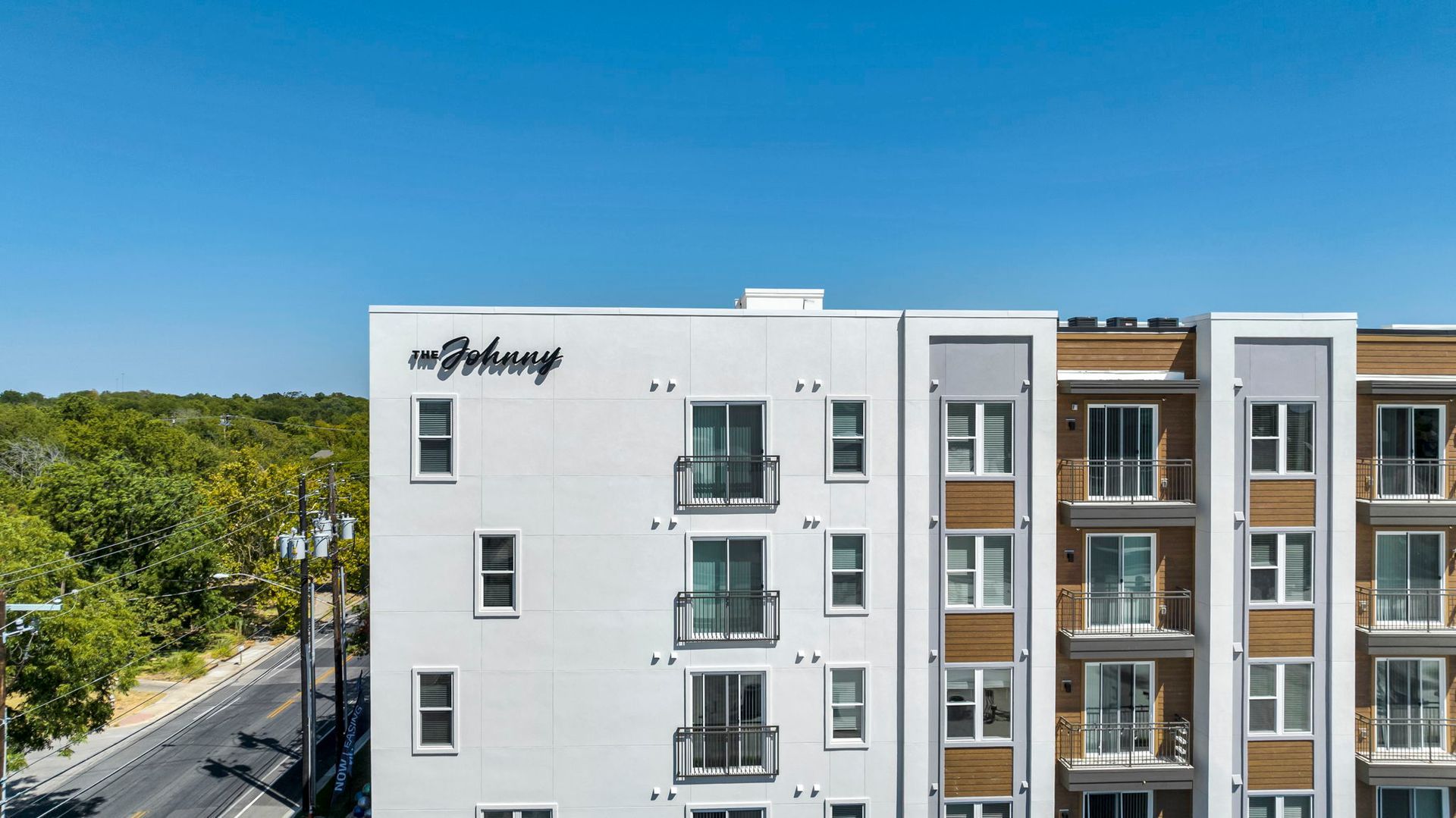 Modern apartment building with white and gray facades beside a tree-lined street under a clear blue sky