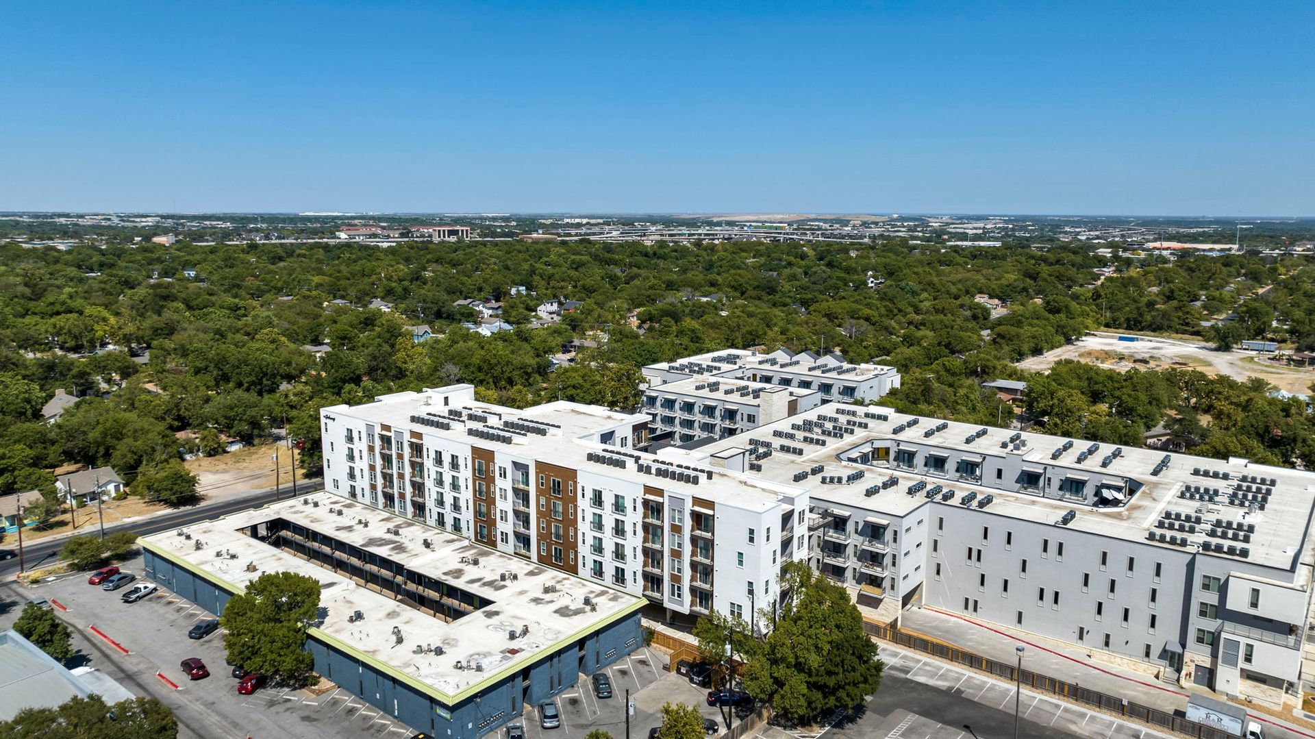 Aerial view of a modern white apartment complex surrounded by trees under a clear blue sky.