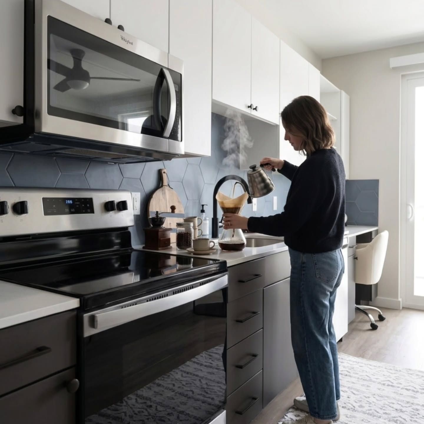 Person using a coffee maker in a modern kitchen with black appliances and white cabinets