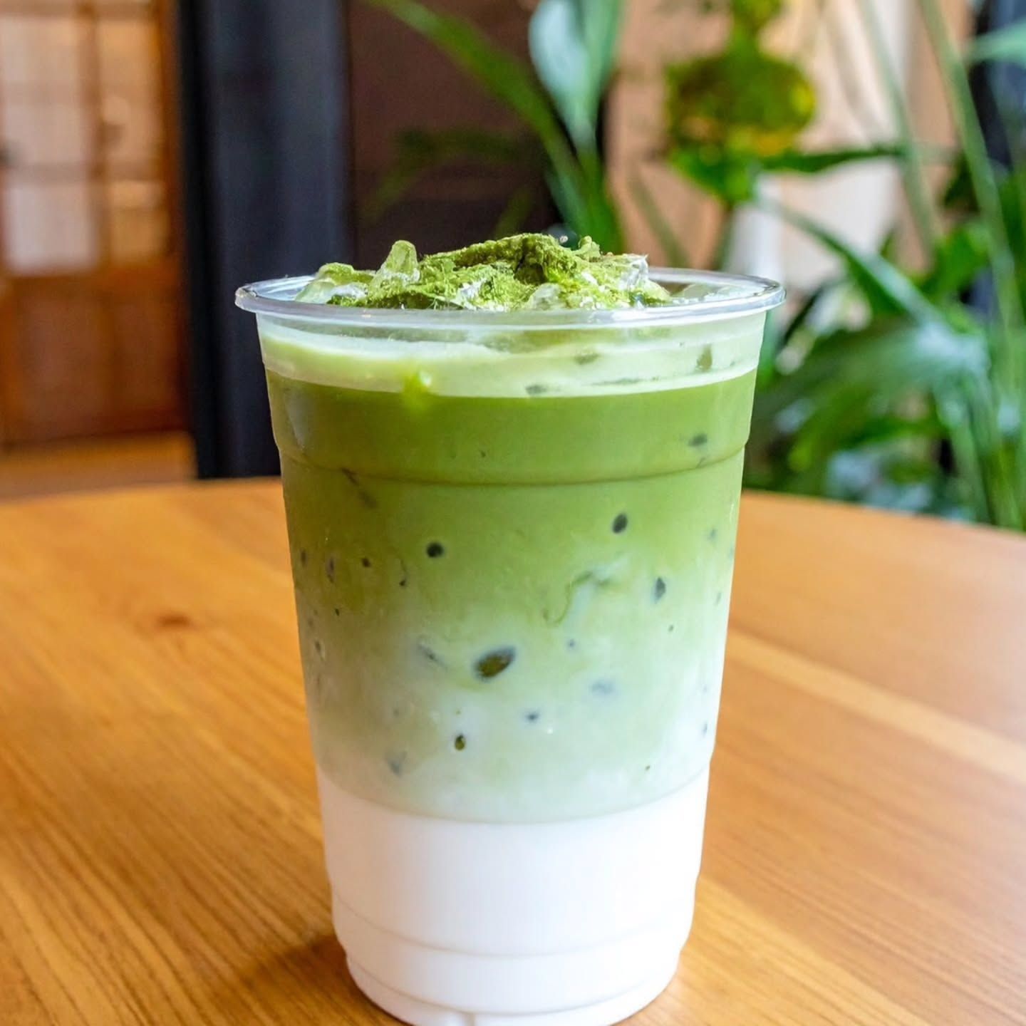 Iced matcha latte in a clear cup on a wooden table, topped with green powder.
