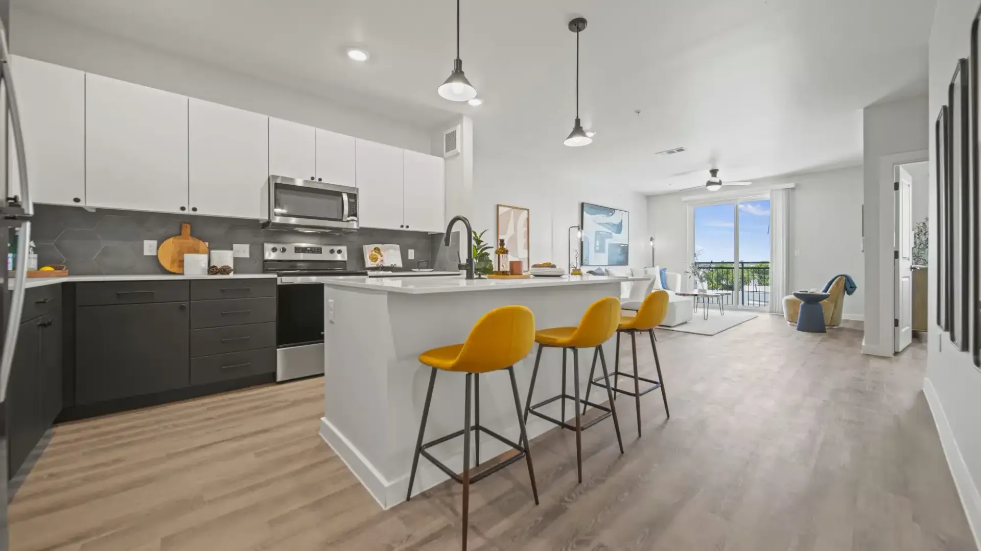 Modern open-plan kitchen and living room with white island, dark cabinets, yellow bar stools, and light wood floors
