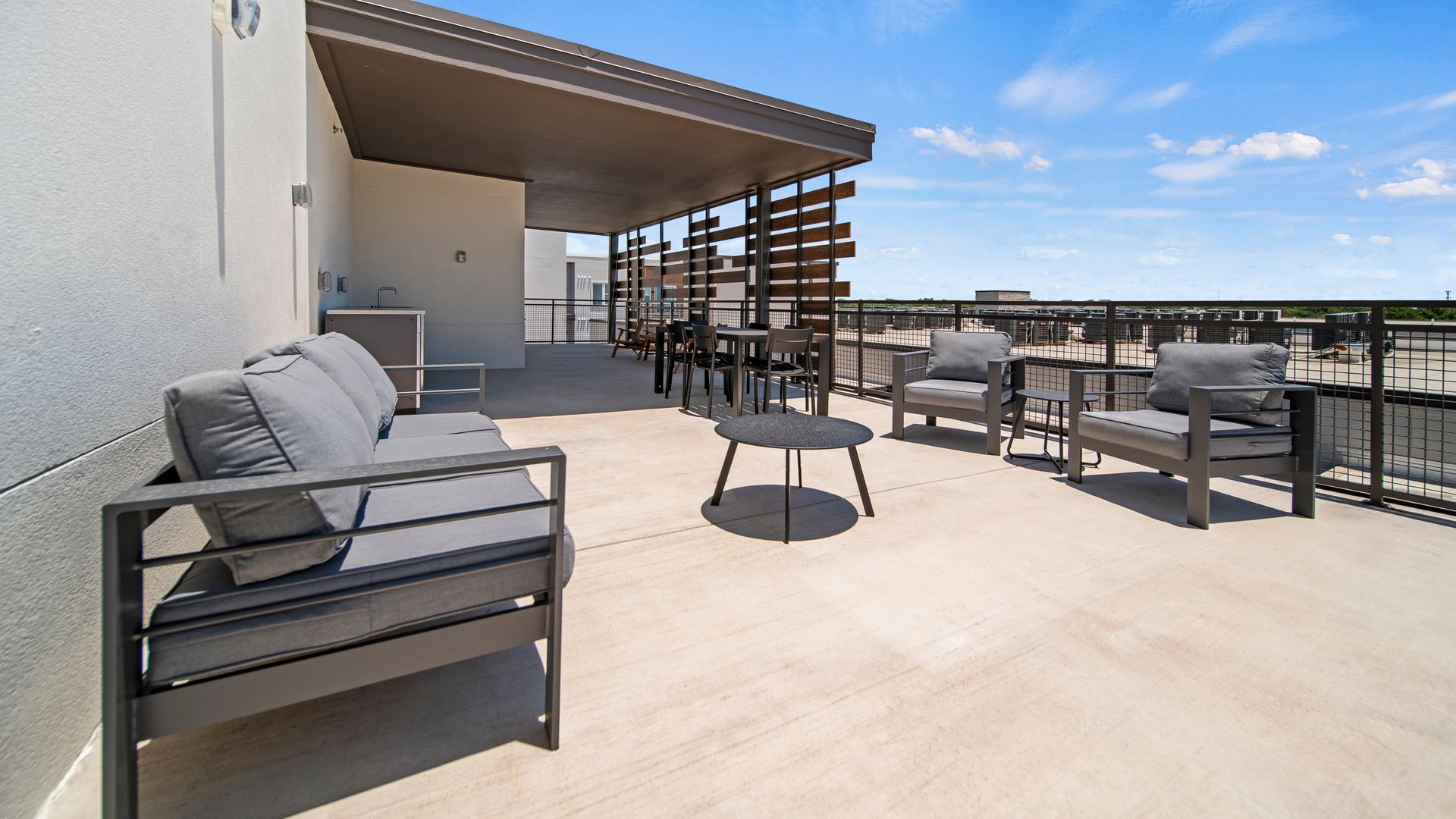 Rooftop patio with gray seating, tables, and city views under a clear blue sky