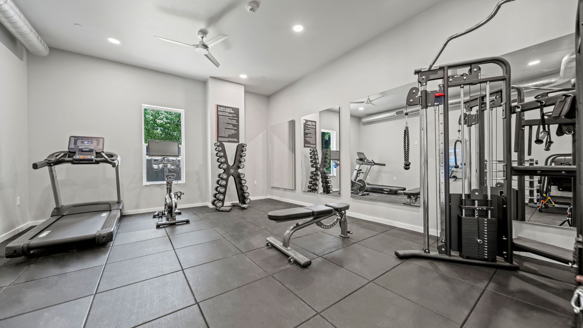 Bright modern home gym with treadmill, weight bench, cable machine, and mirrored walls