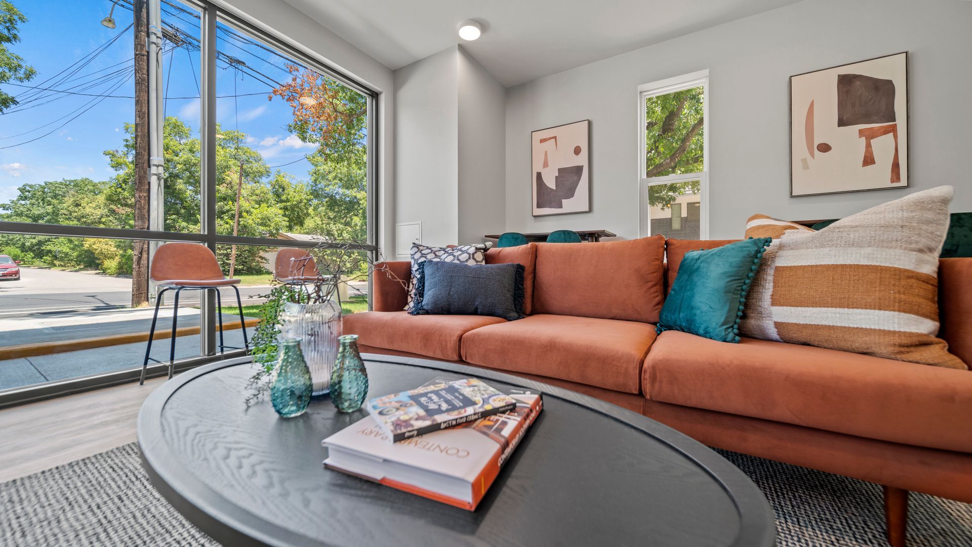 Bright modern living room with orange sofa, round coffee table, and large windows overlooking greenery
