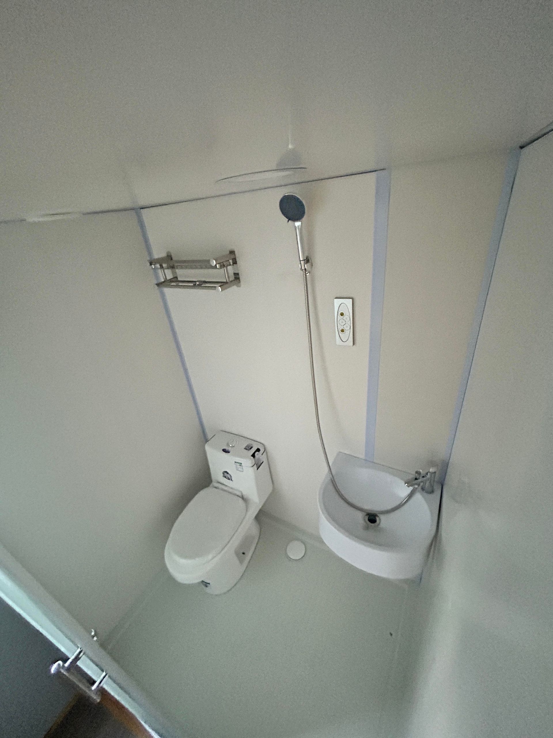 Small bathroom with toilet, bidet, and handheld shower against tiled walls.