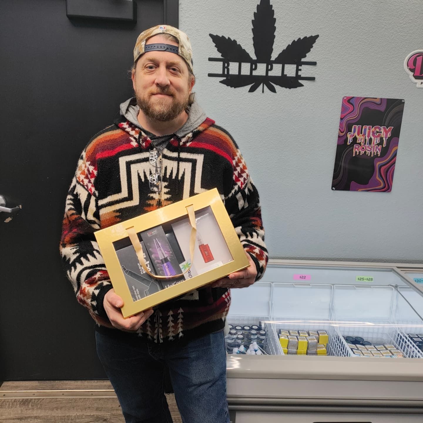 Man in patterned sweater holding a gift box in a cannabis dispensary.