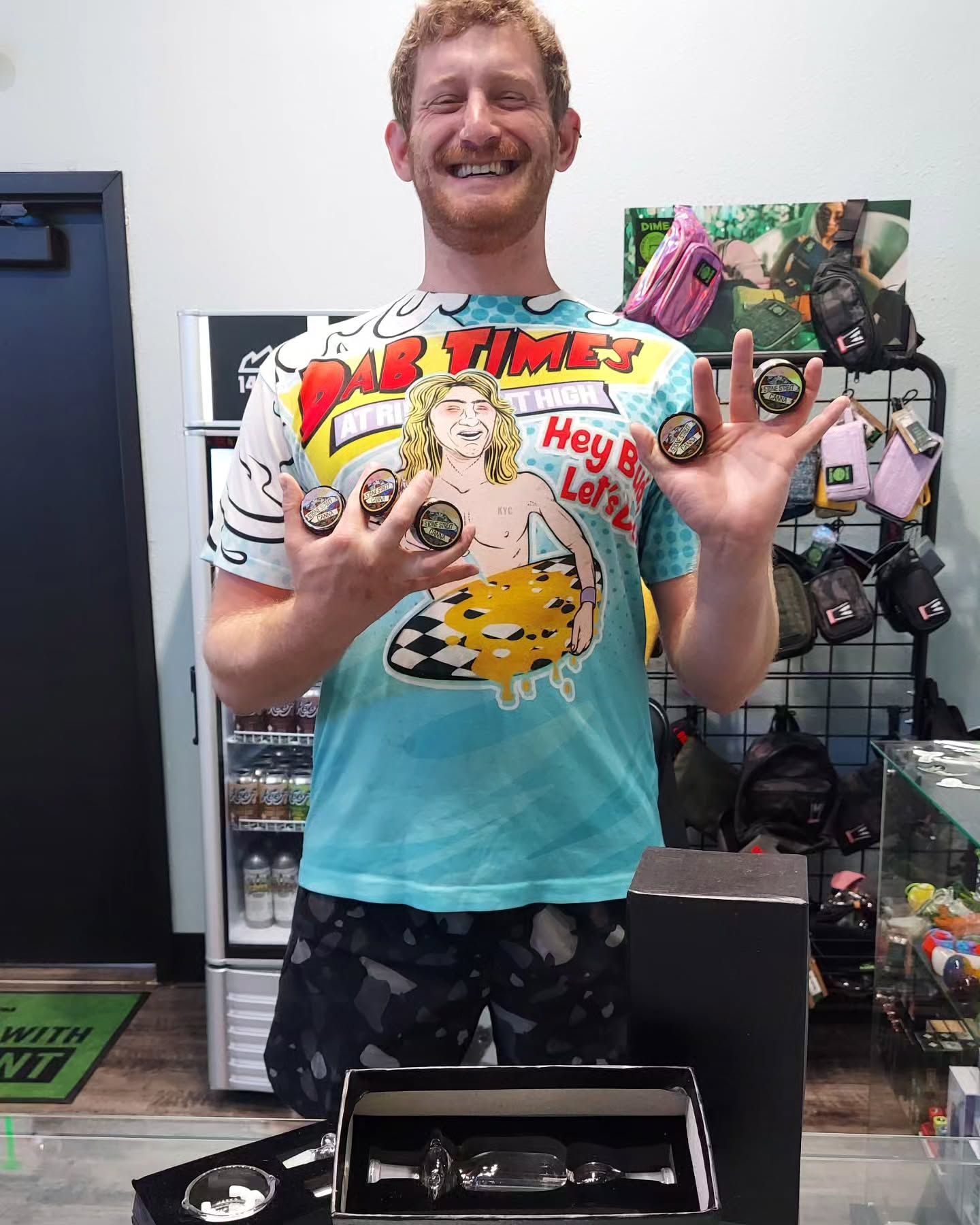 Man holding three small items, smiling in a store. Items are round, in front of a counter with a box.