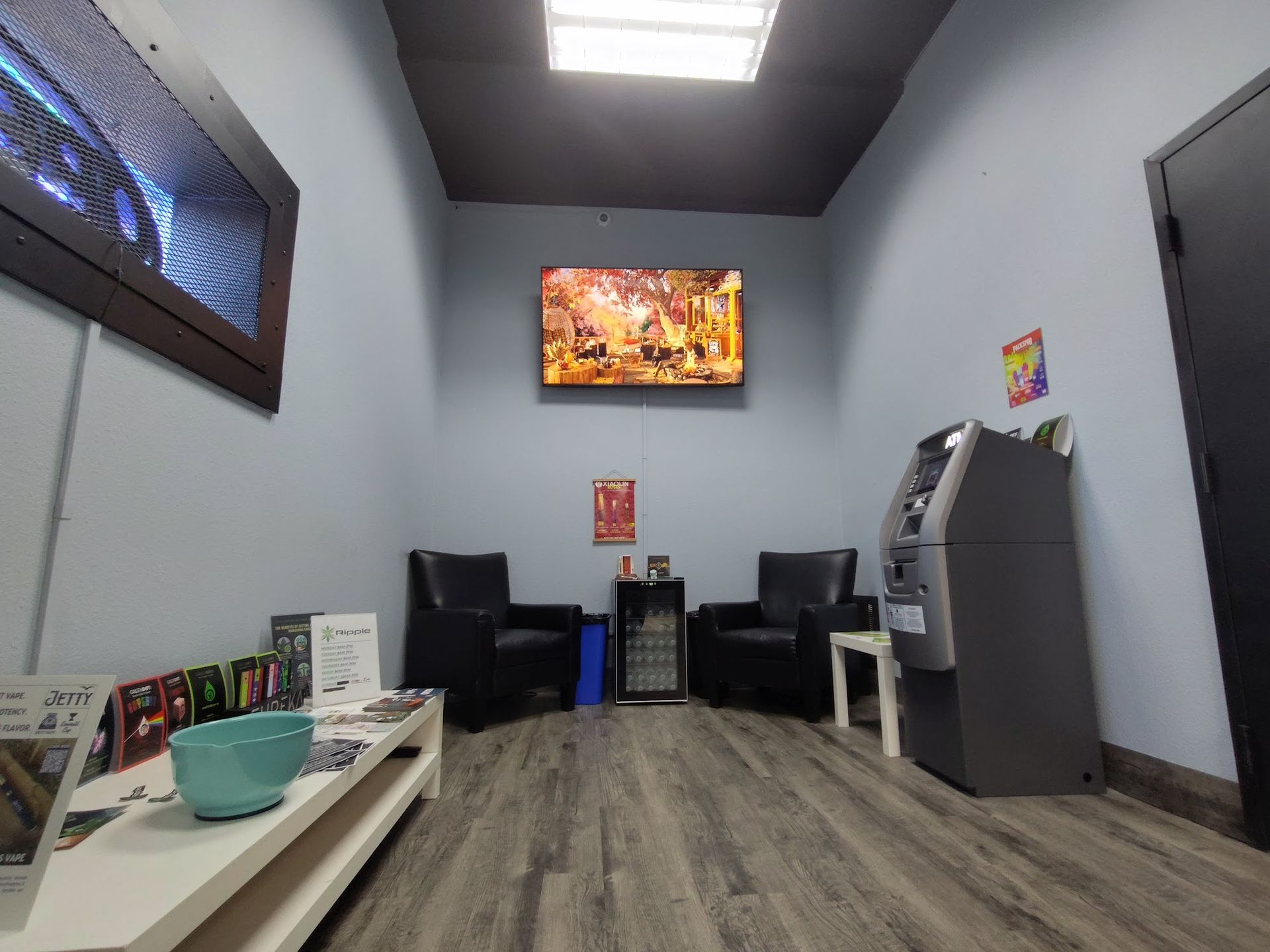Waiting room with ATM, chairs, TV, and low table with display.