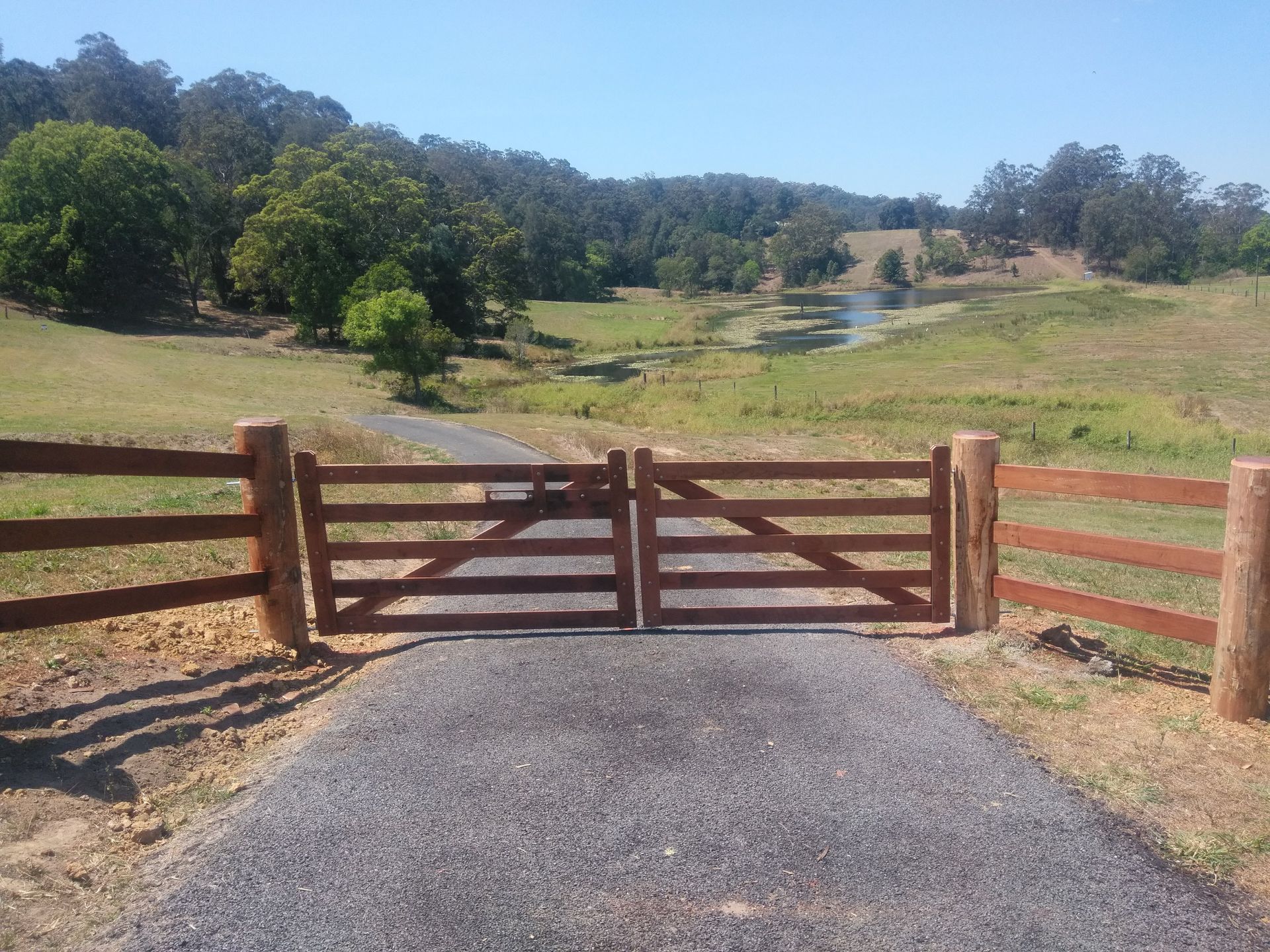 A Wooden Fence and Gates in Front Of A Driveway Surrounded by Grass — John Stark Fencing In West Woombye, QLD