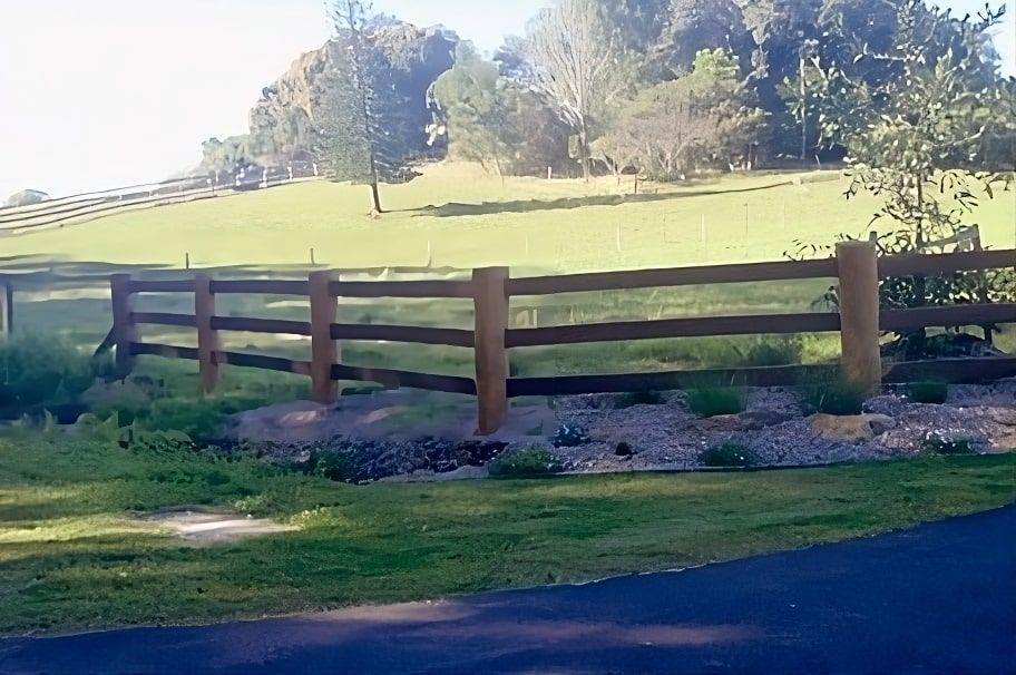 A Wooden Fence Surrounds A Grassy Field With Trees In The Background — John Stark Fencing In Bli Bli, QLD