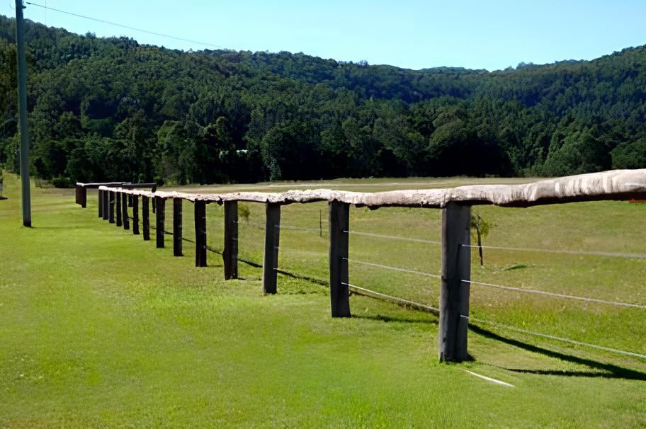 A Long Wooden Fence Surrounds A Grassy Field With Mountains In The Background — John Stark Fencing In Bli Bli, QLD