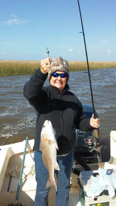 Person on a boat holding up a large fish, with fishing rod and marshland in the background.