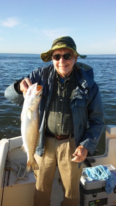 Person on a boat holding a large fish, wearing a hat and sunglasses on the open water.