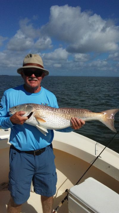 Man in blue shirt and hat holding a large fish on a boat with open water and cloudy sky behind him