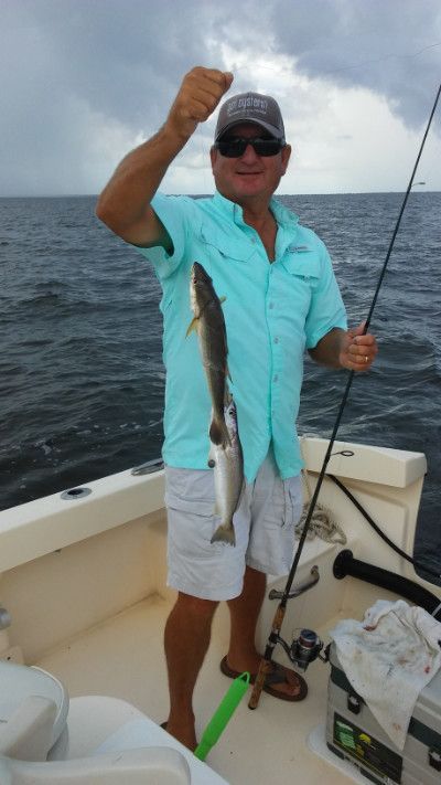 Man on a boat holding up a fish he caught, with the ocean and cloudy sky behind him.