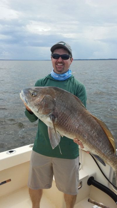 Man holding a large fish on a boat with open water in the background