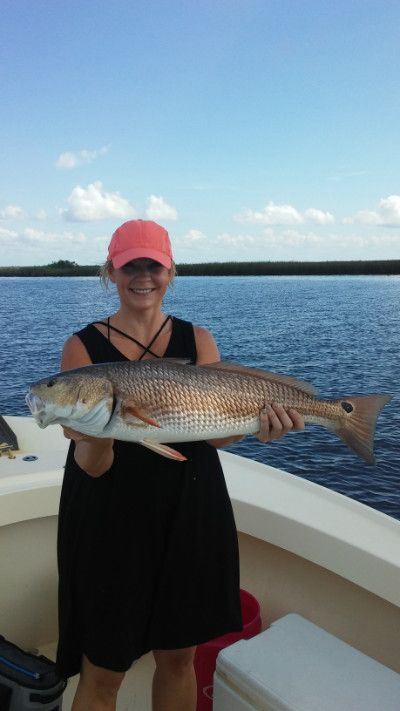 Person in a pink cap holding a large fish on a boat over blue water under a sunny sky