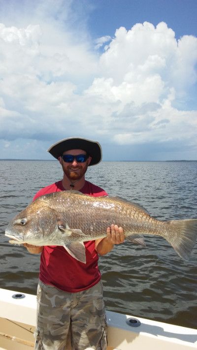 Man holding a large fish on a boat, with water and cloudy sky in the background.