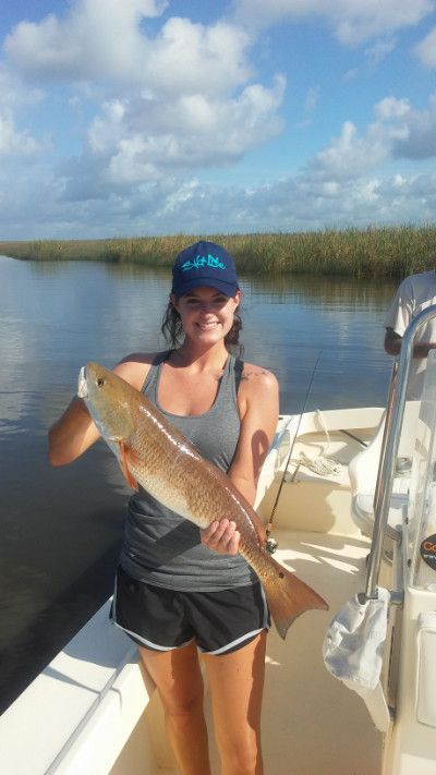 Woman holding a large fish on a boat in calm marsh waters under a cloudy sky