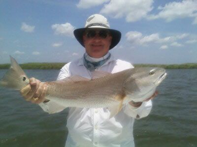 Person in a hat holding a large fish on a boat with water and blue sky in the background.