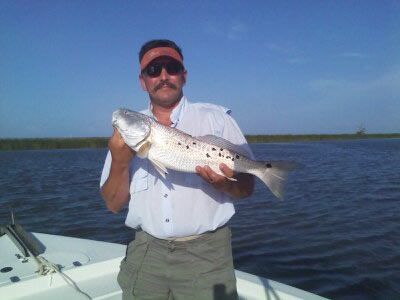 Man holding a large silver fish on a boat in calm blue water under a clear sky