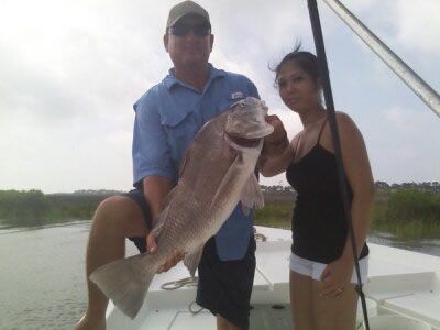 Two people on a boat holding a large fish over the water.