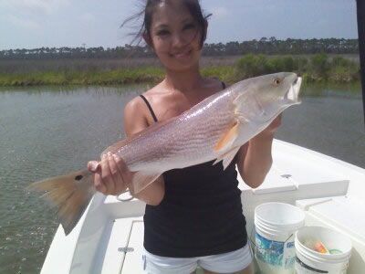 Person holding a large silver fish on a boat with water and marshland in the background