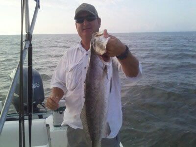 Man on a boat holding up a large fish over the water at sea