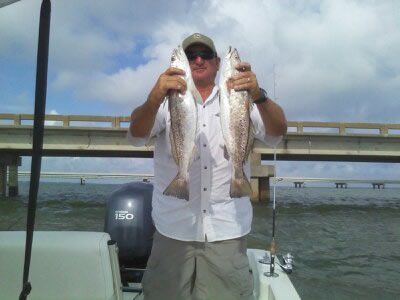 Person holding two fish on a boat near a bridge over calm water