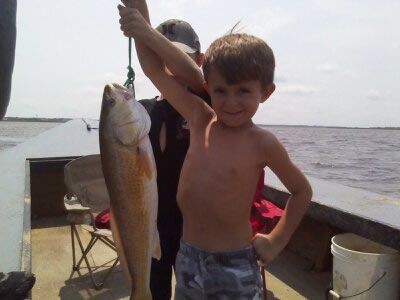 Child on a boat holding up a large fish by the shore