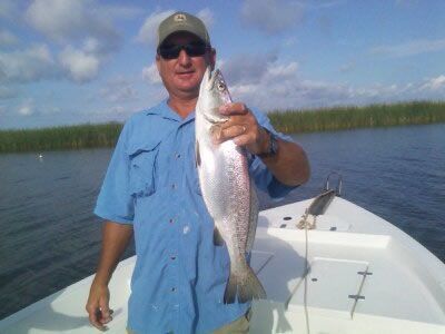 Man on a boat holding a large fish on a lake under a blue sky