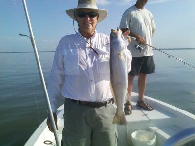 Two anglers on a boat, one holding a large fish on a calm blue sea.