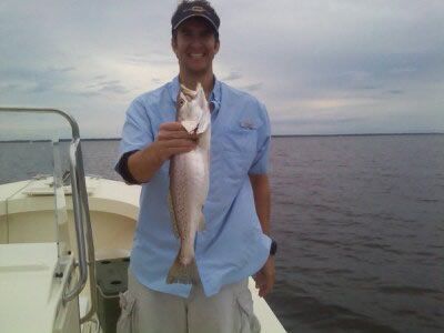 Person on a boat holding a large fish over the water at dusk.
