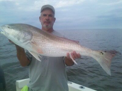 Man on a boat holding a large silver fish over calm water at dusk