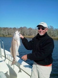Man on a boat holding a large fish beside calm water under a clear blue sky