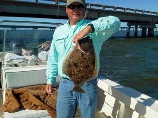 Man on a boat holds up a large flat fish with a bridge and water in the background
