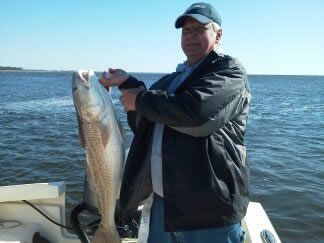 Person holding a large fish on a boat with open water in the background