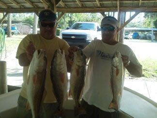 Two people holding large fish at a picnic shelter with a parked truck in the background