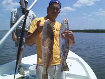 Two people on a boat hold large fish over calm water under a clear sky.
