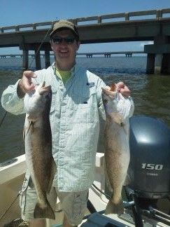 Person on a boat holding two large fish near a bridge on the water.