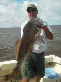 Person holding a large fish on a boat, with water and cloudy sky in the background.