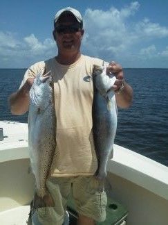Person on a boat holding two large fish against the ocean background